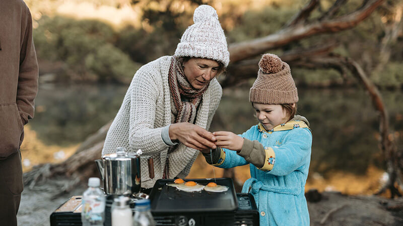 Mother and daughter fry eggs by their campsite