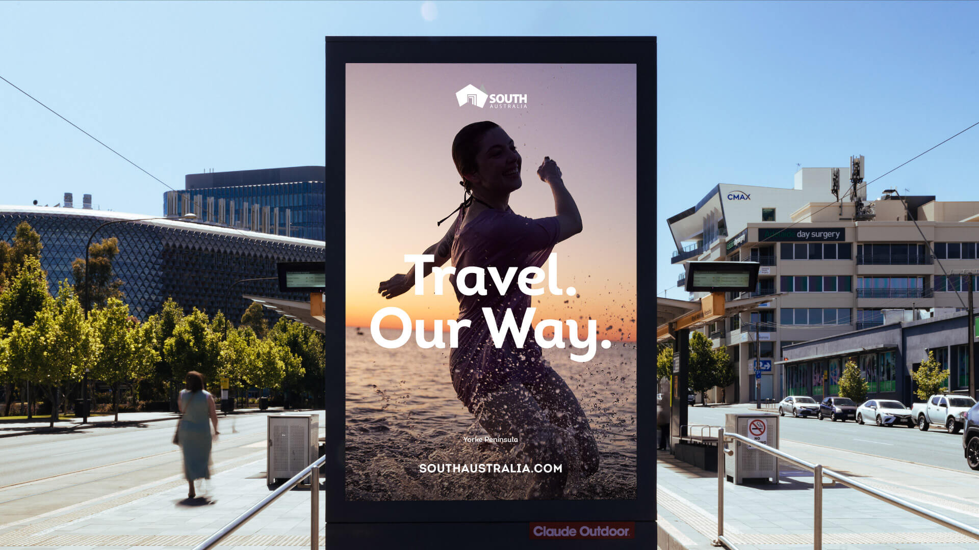 Outdoor signage displaying the 'Travel Our Way' tagline against a photo of a sunset silhouetted figure at the beach.